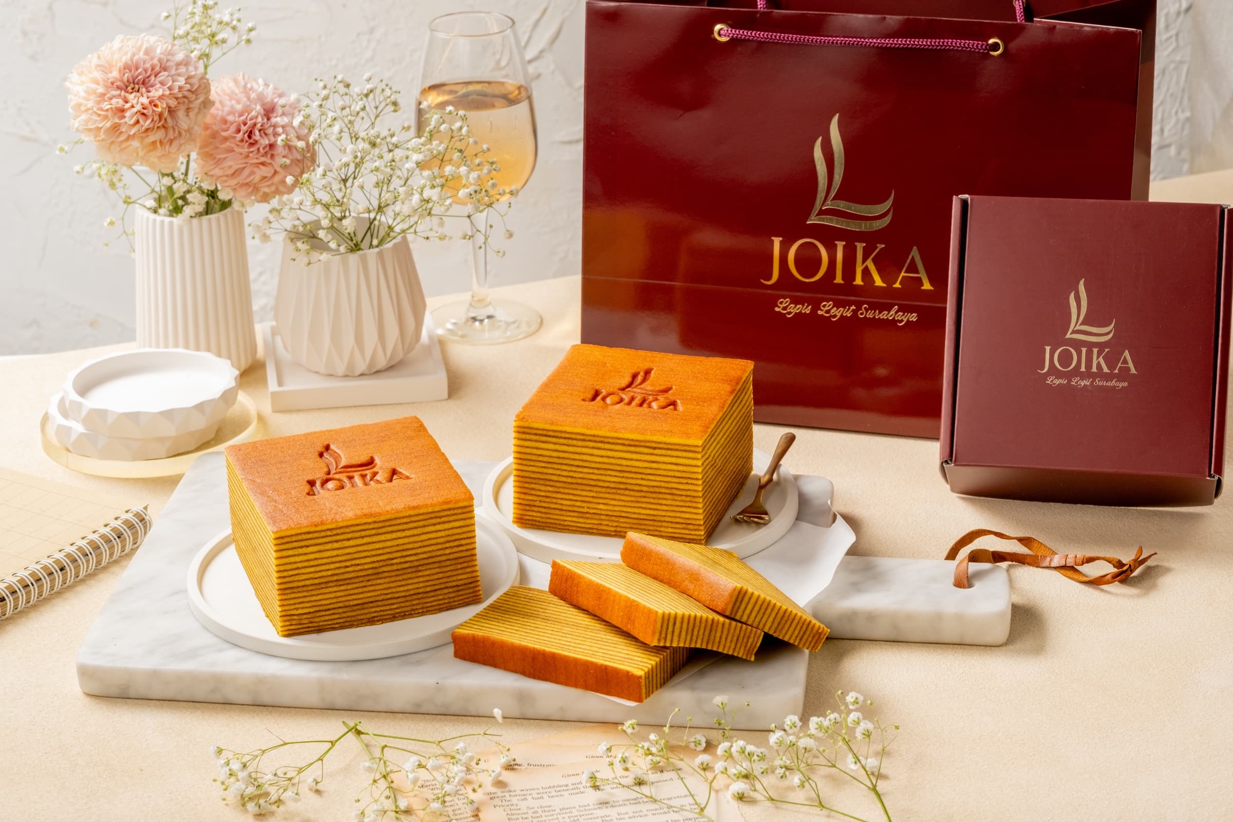 Lapis Legit Joika dan kemasan hadiah berwarna merlot di atas meja.